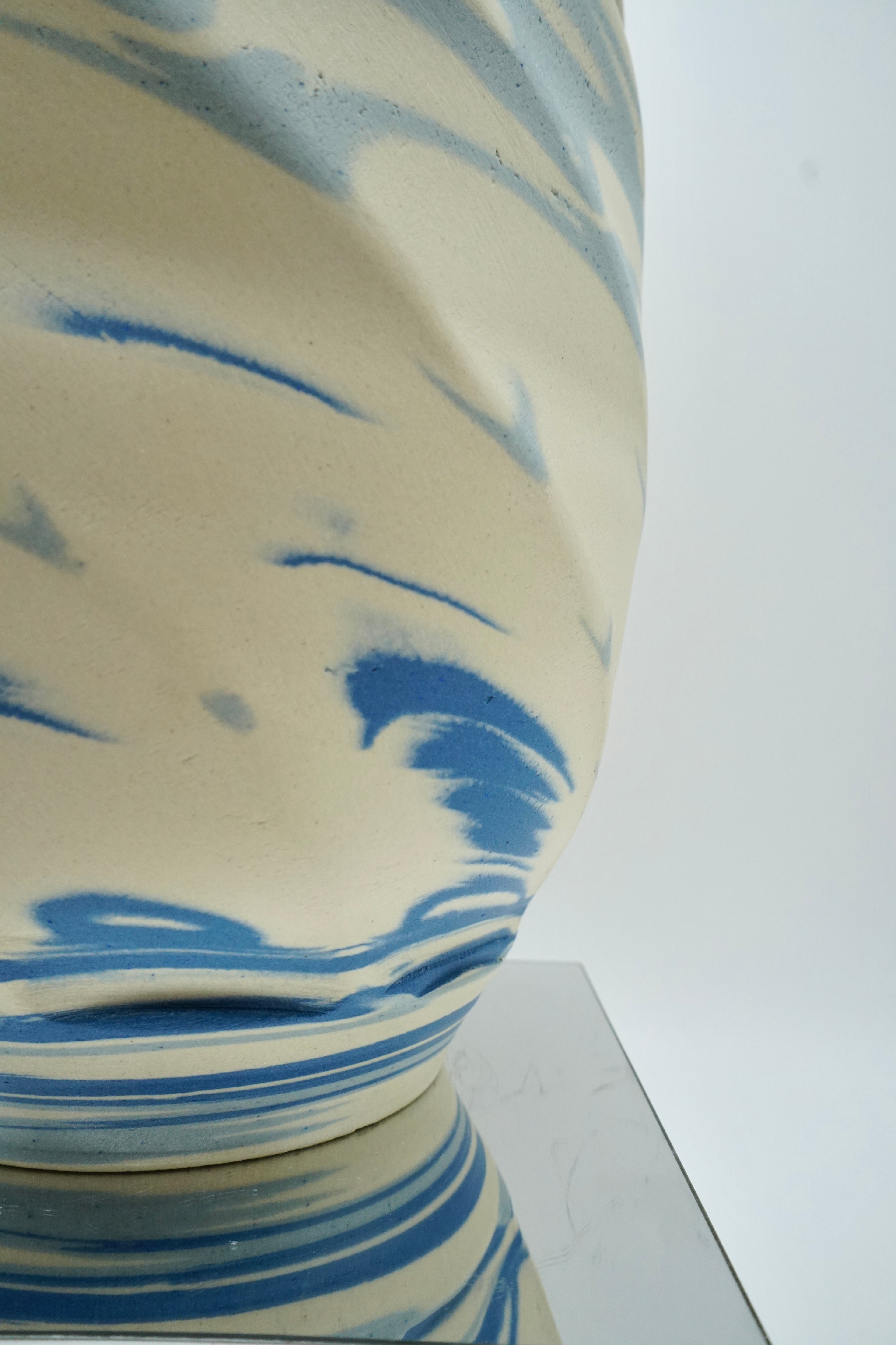Ceramic vase with blue and white abstract design on a reflective surface and white background