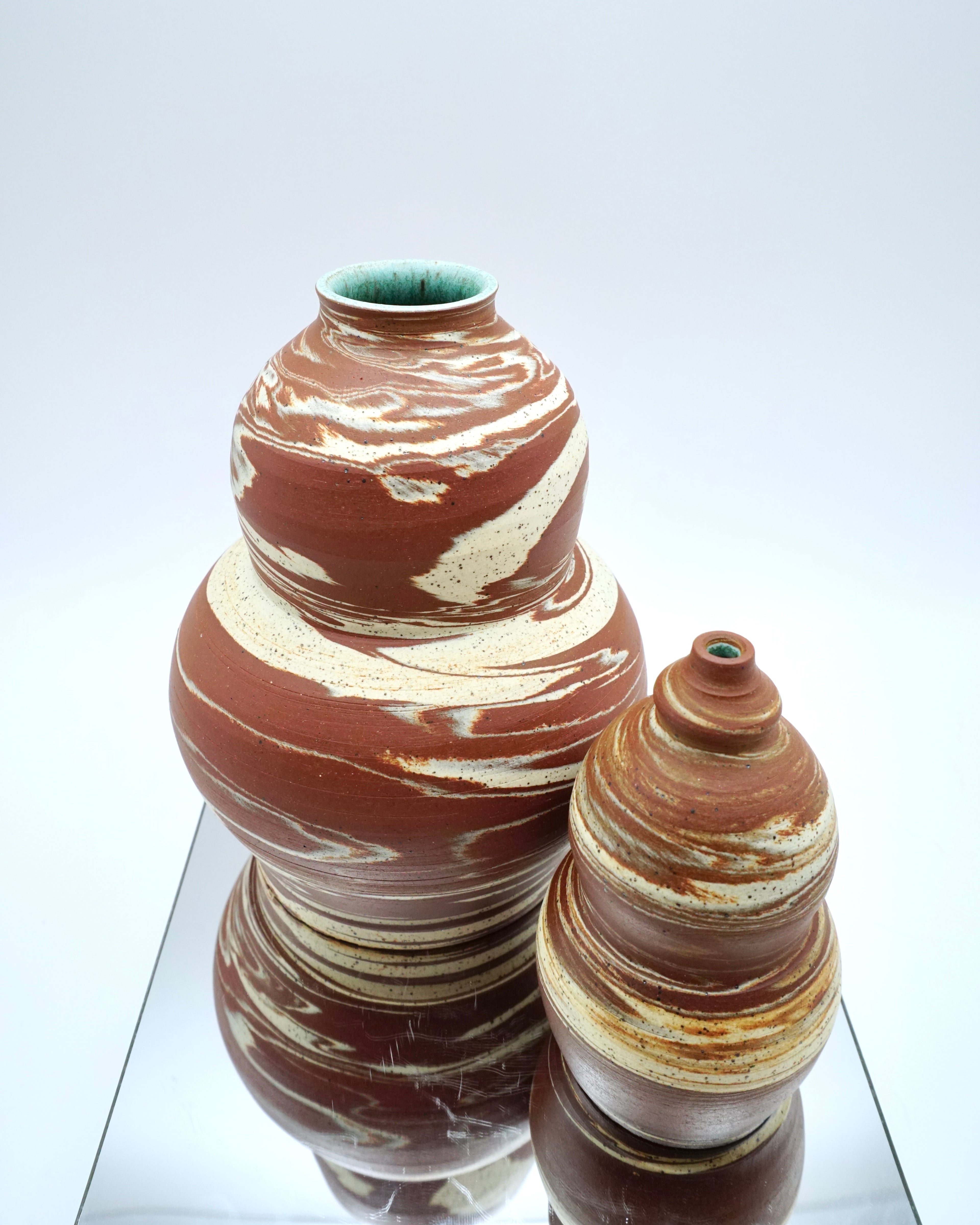 Two ceramic vases with marbled patterns on a reflective surface and white background