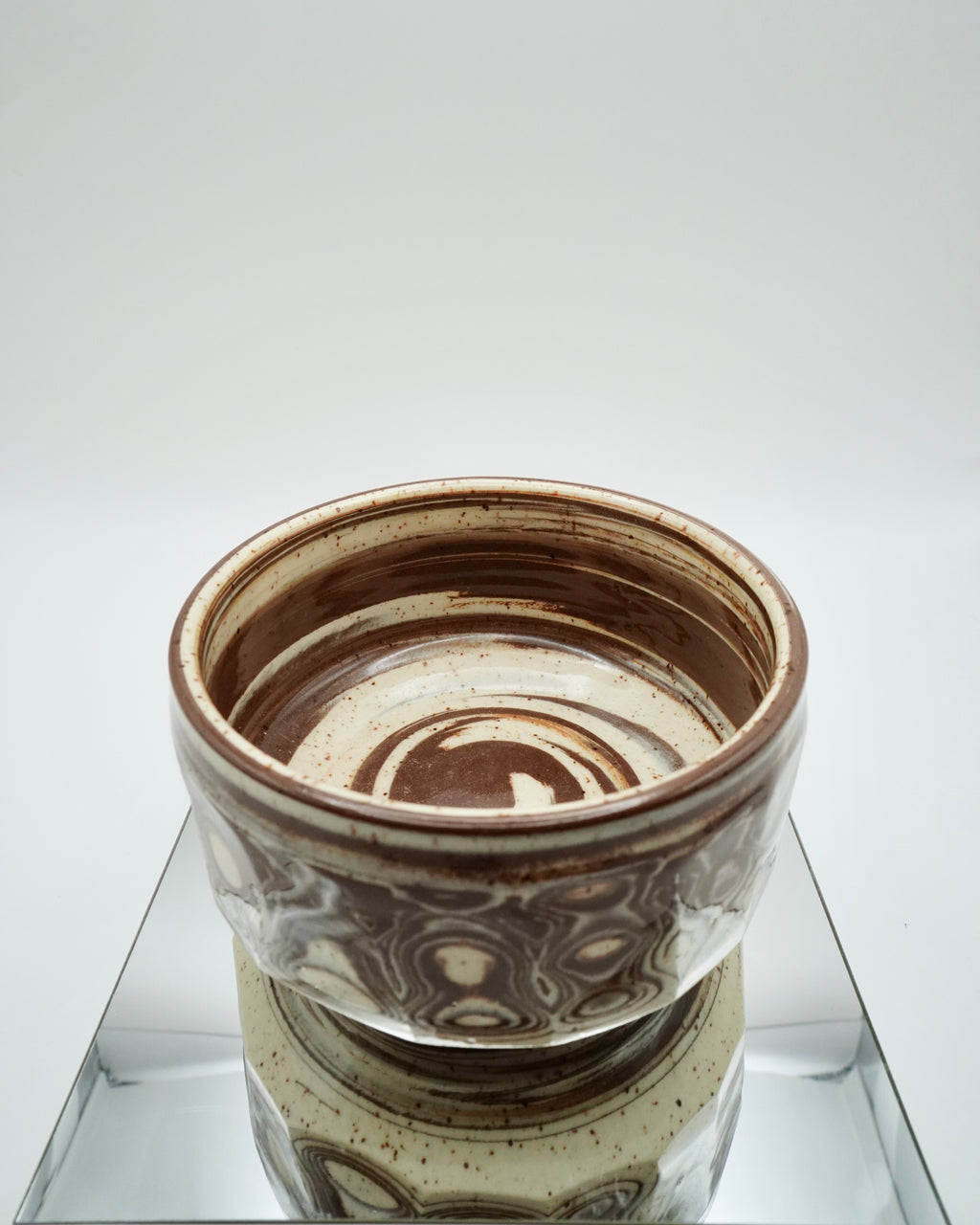 Ceramic bowl with brown and speckled white patterns on a reflective surface and white background.