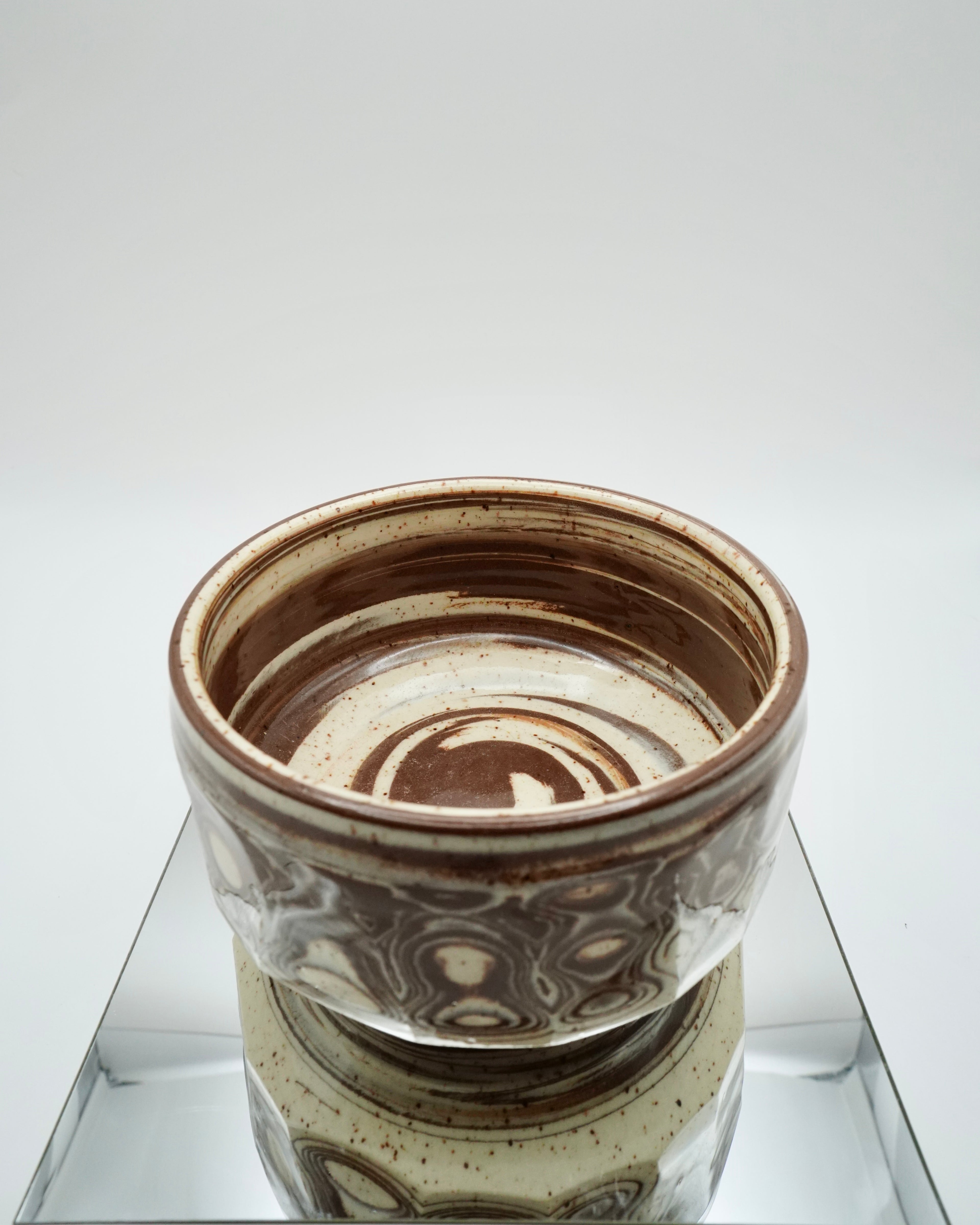 Ceramic bowl with brown and speckled white patterns on a reflective surface and white background.