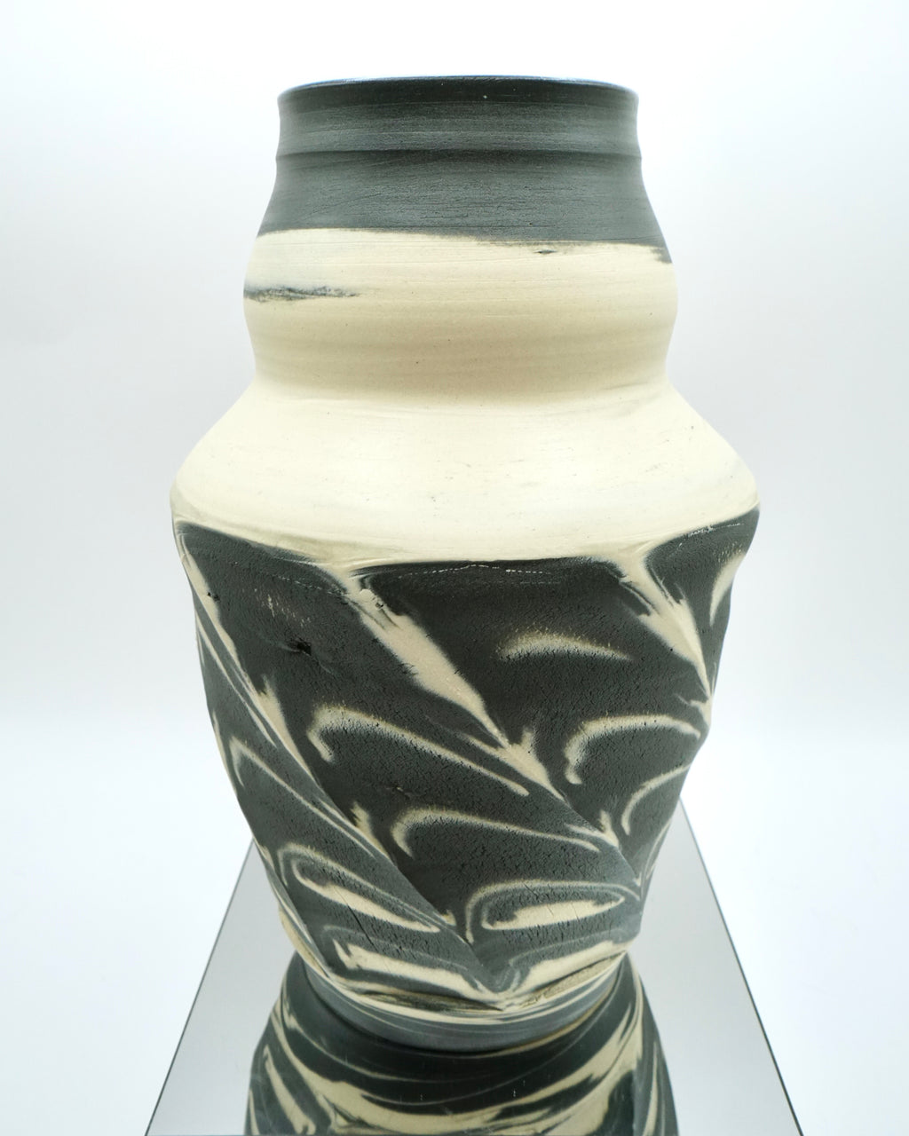 Ceramic vase with black and white marbled pattern on a reflective surface and white background