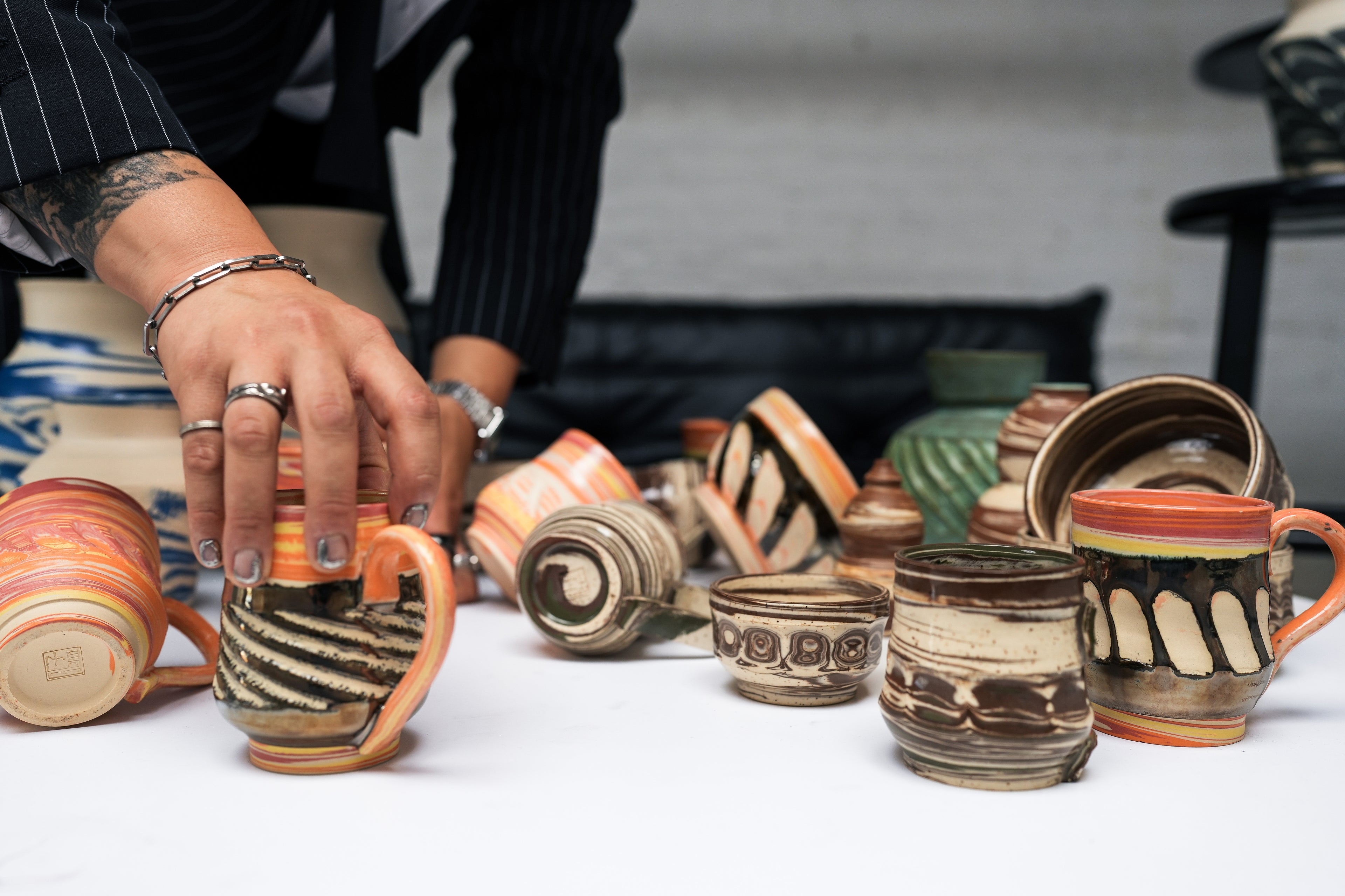 Person arranging various ceramic cups with intricate designs on a white surface.