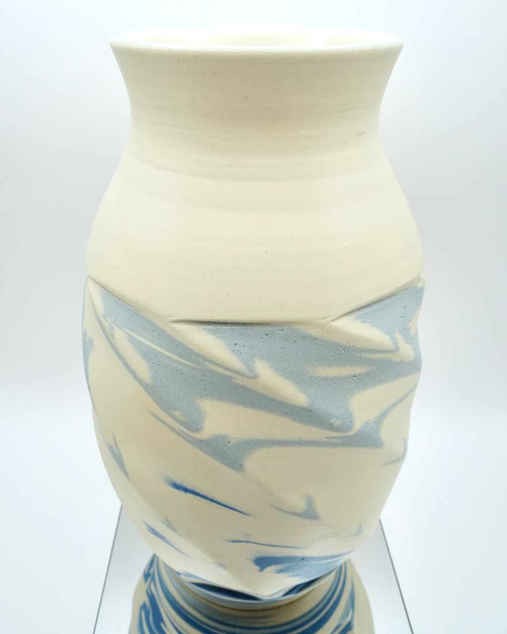 Ceramic vase with blue and white abstract pattern on a reflective surface and white background