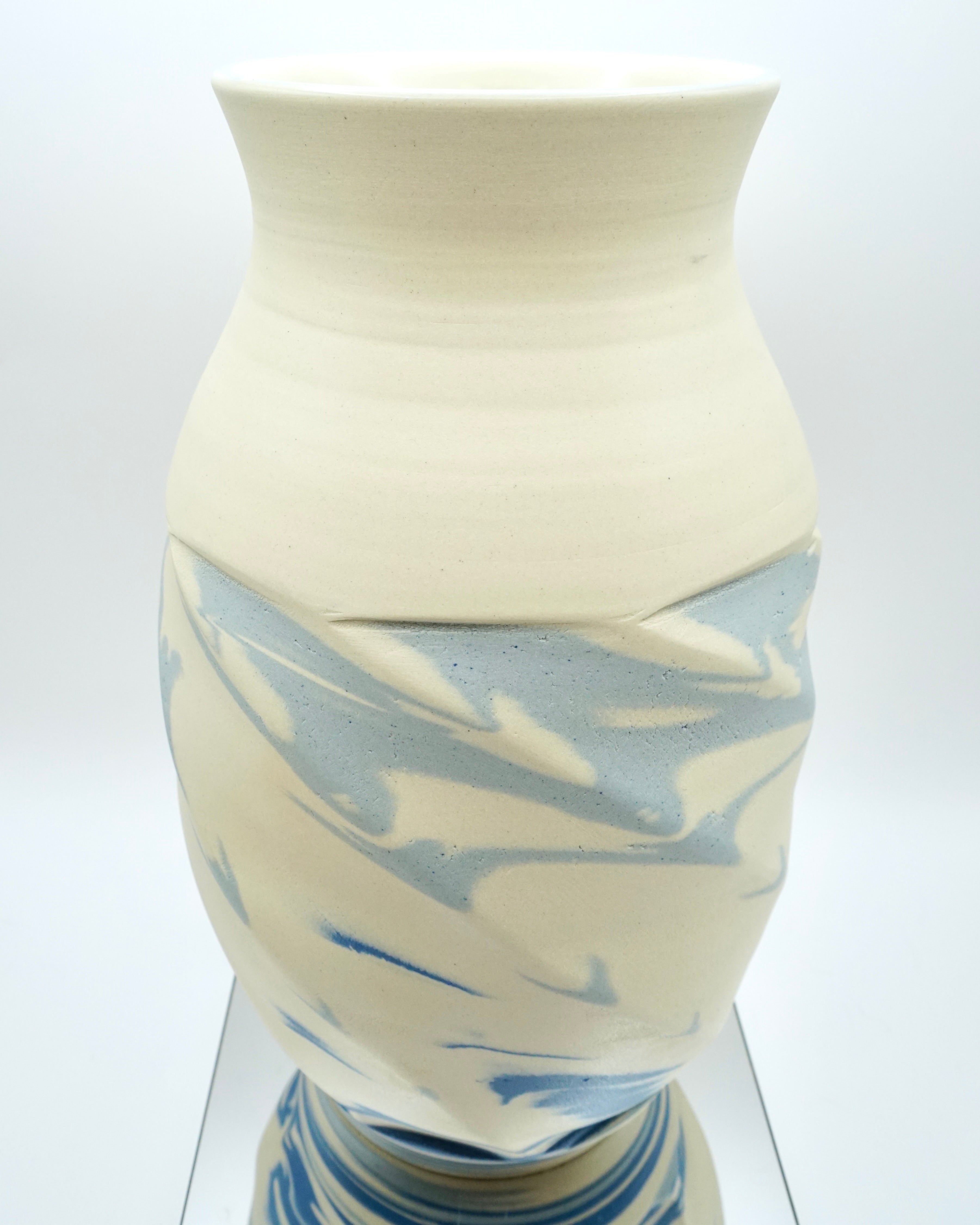 Ceramic vase with blue and white abstract pattern on a reflective surface and white background