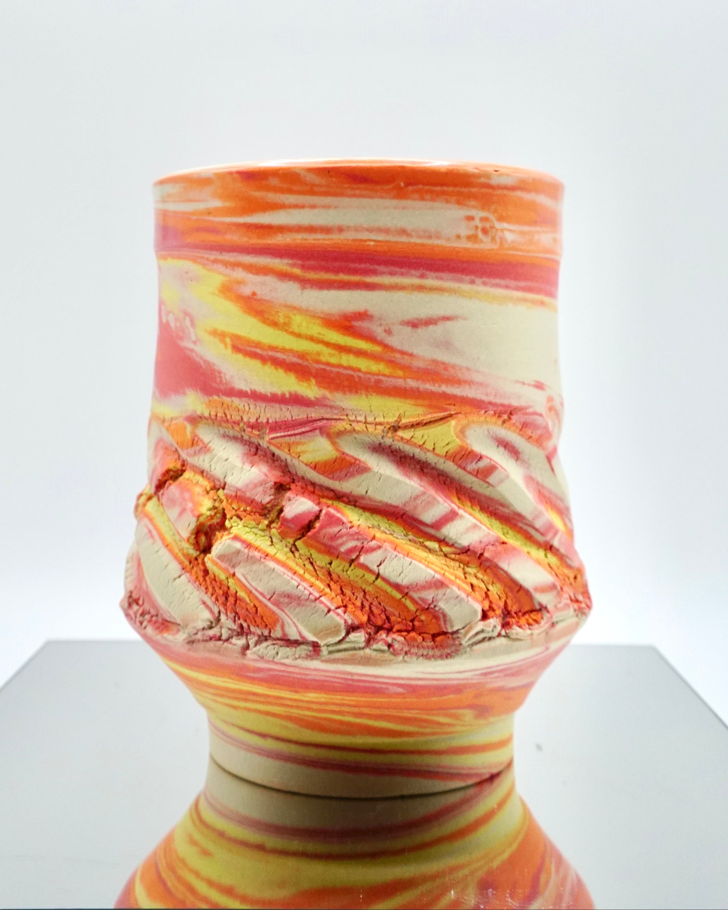 Ceramic cup with red, orange, yellow, white swirled patterns on a reflective surface and white background.