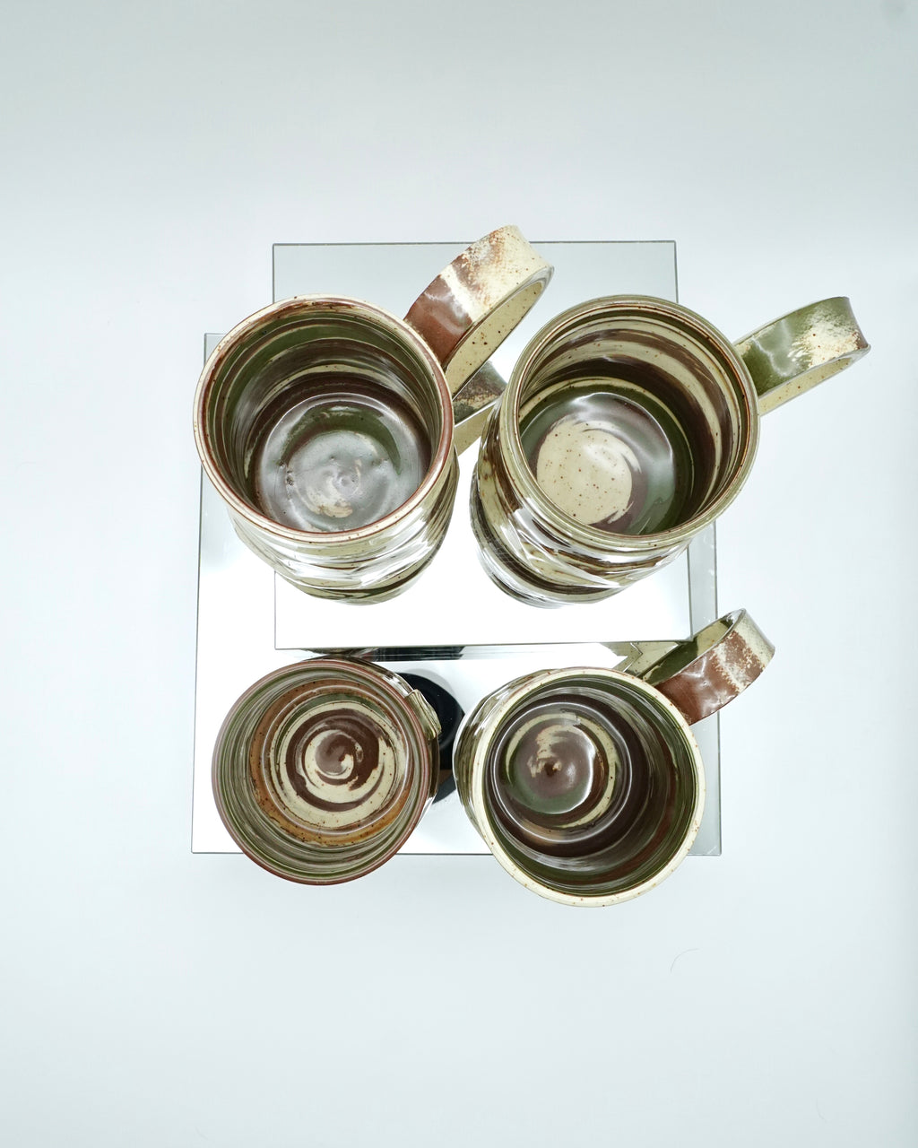 Set of four ceramic mugs with brown, green, and speckled white abstract patterns on reflective surfaces and a white background.