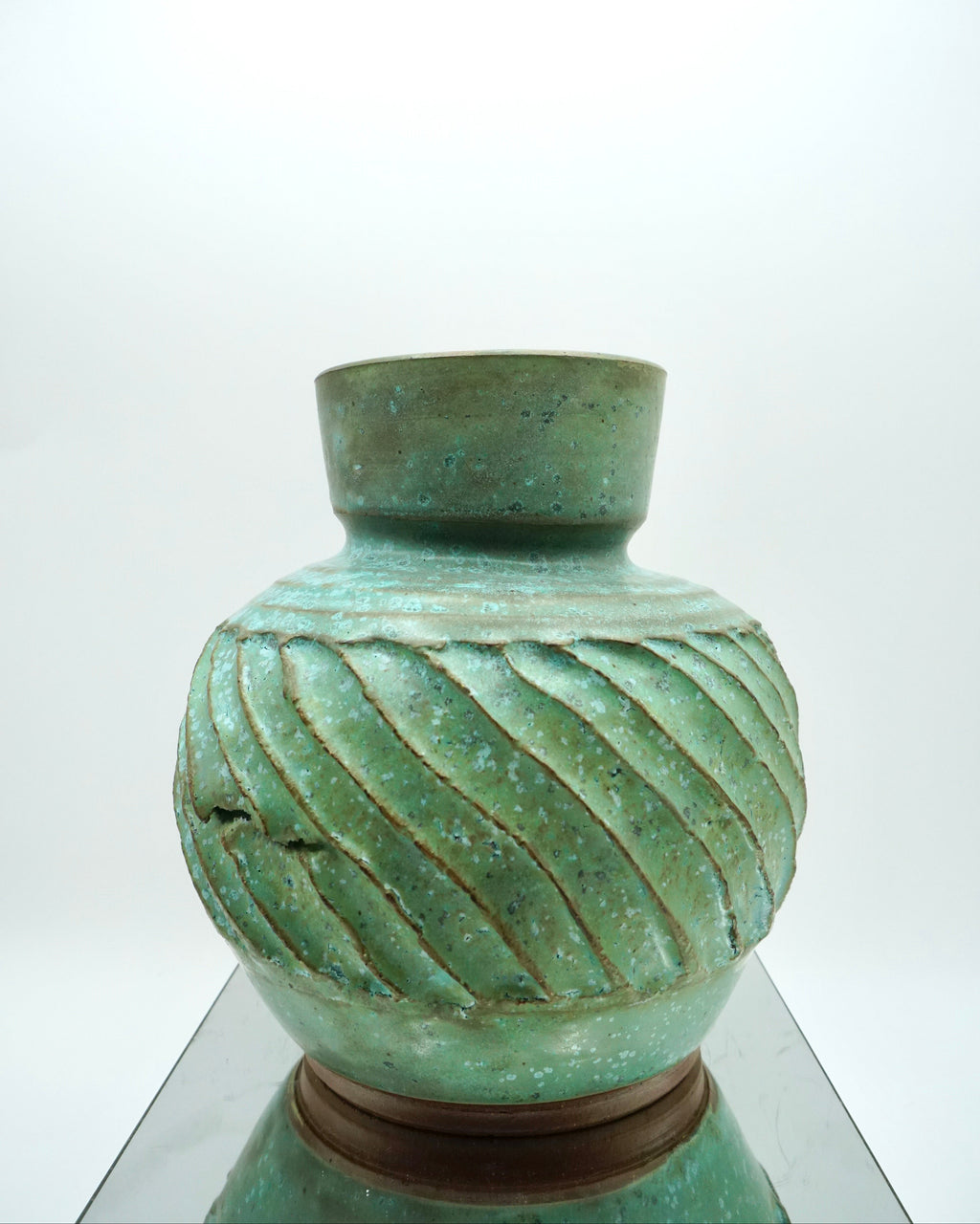 Green ceramic vase with textured design on a reflective surface and white background