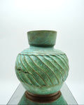 Green ceramic vase with textured design on a reflective surface and white background