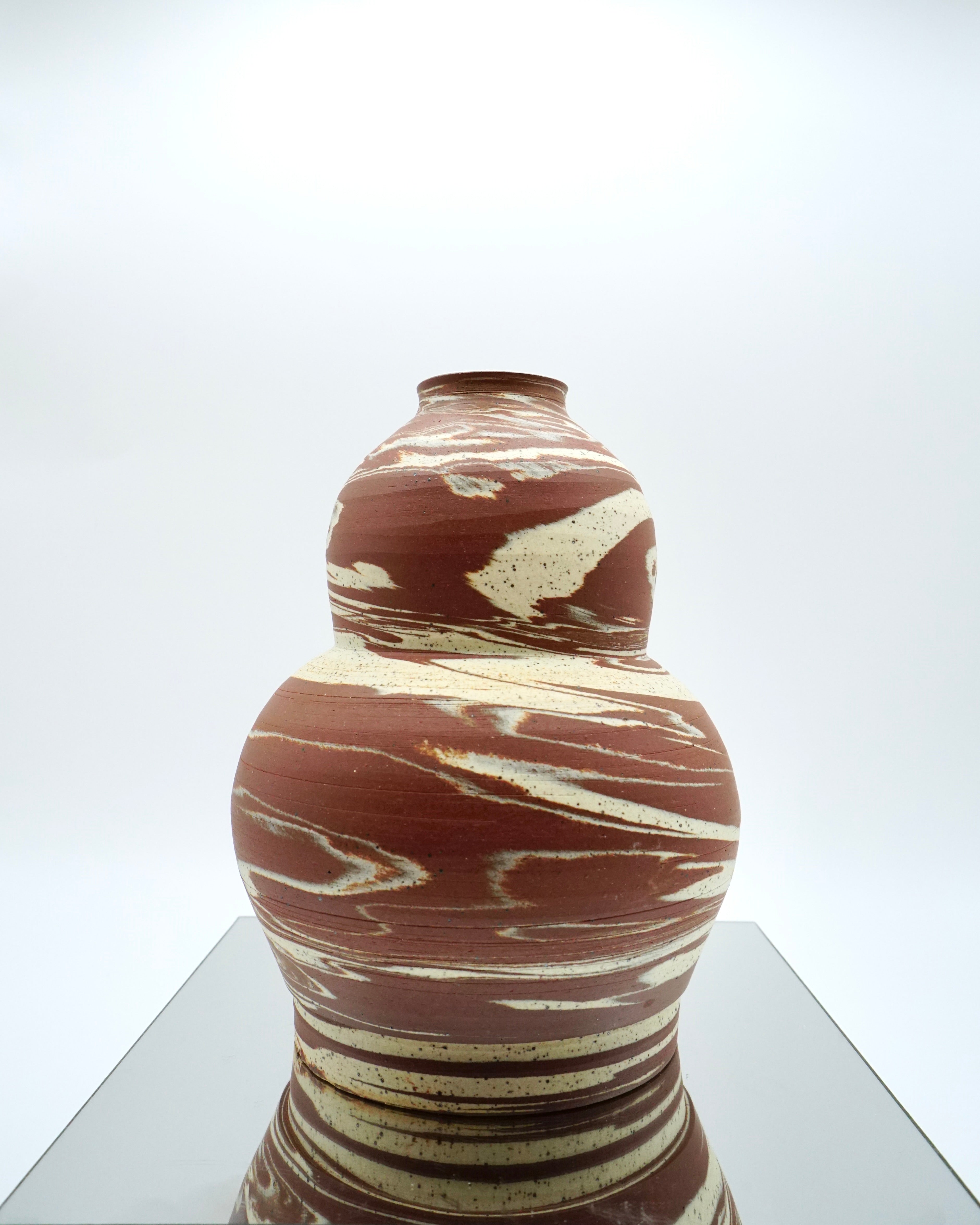 Marbled ceramic vase on a reflective surface with a white background