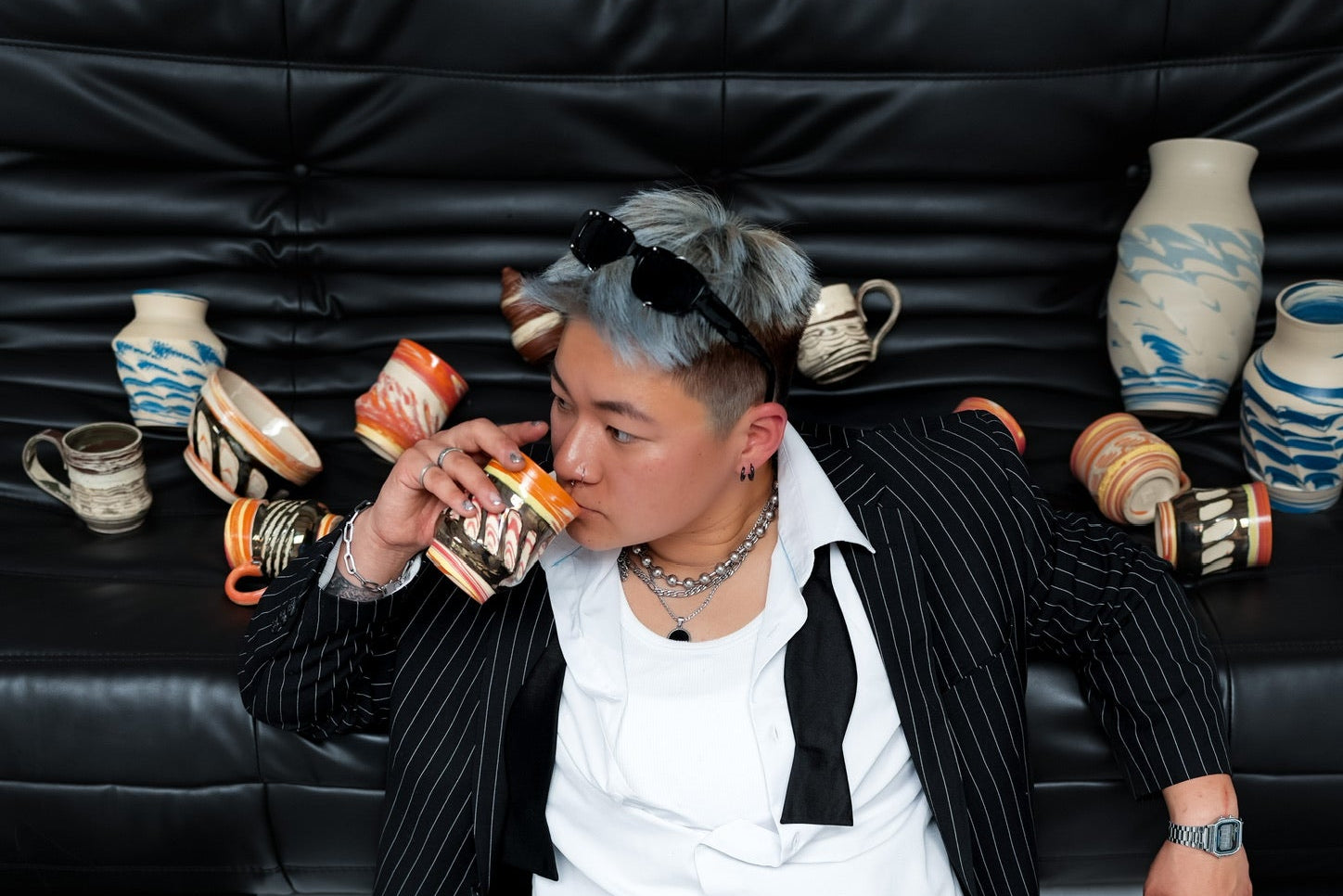 Person in a black pinstripe suit sitting with vases around