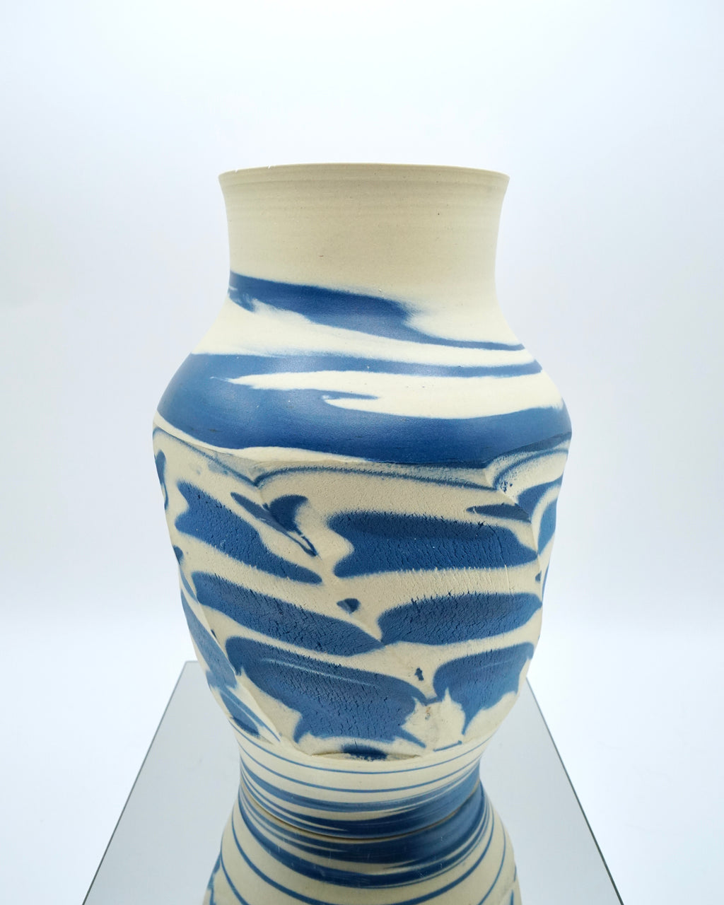 Ceramic vase with blue and white abstract pattern on a reflective surface and white background