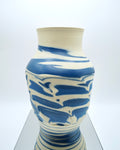 Ceramic vase with blue and white abstract pattern on a reflective surface and white background