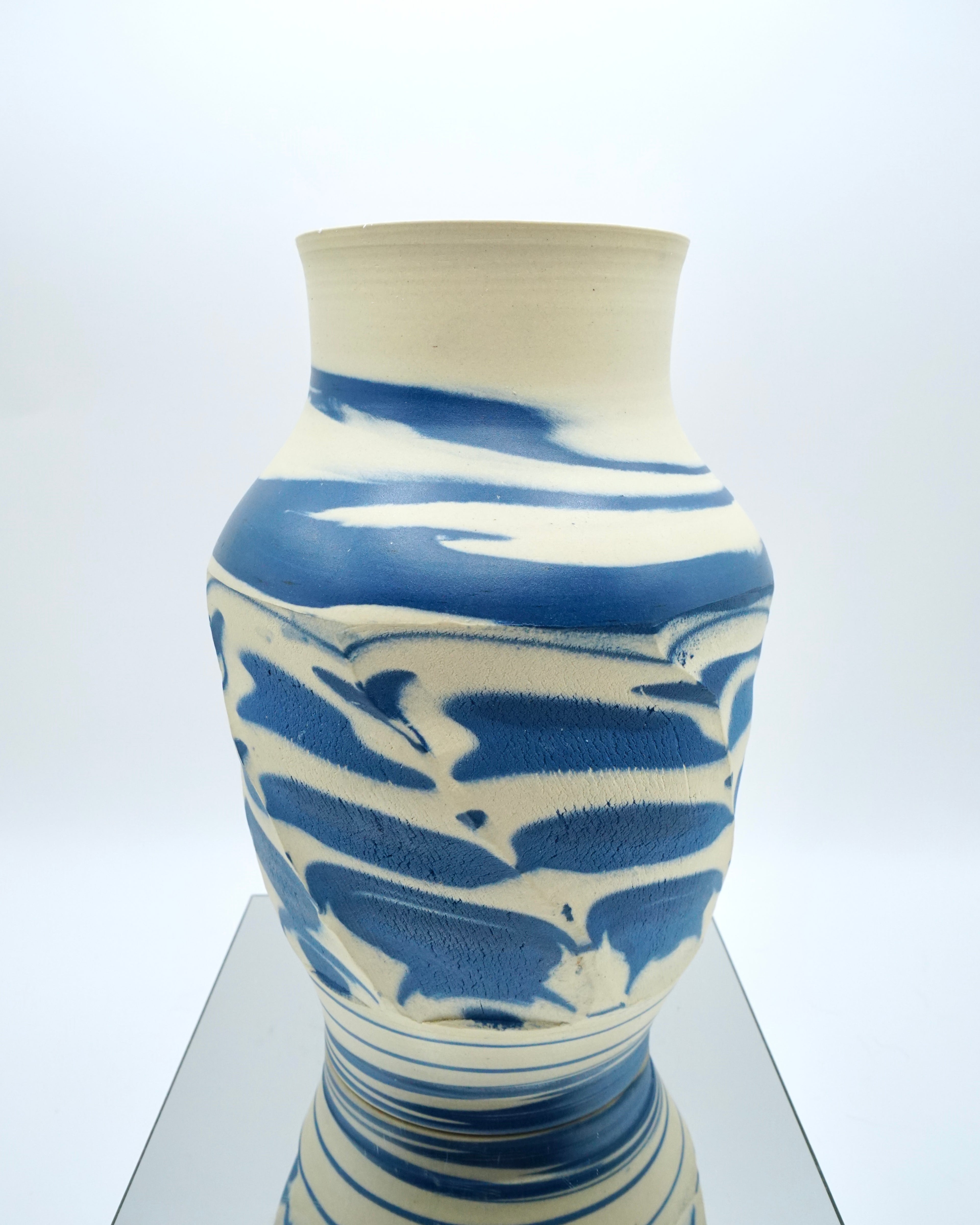 Ceramic vase with blue and white abstract pattern on a reflective surface and white background