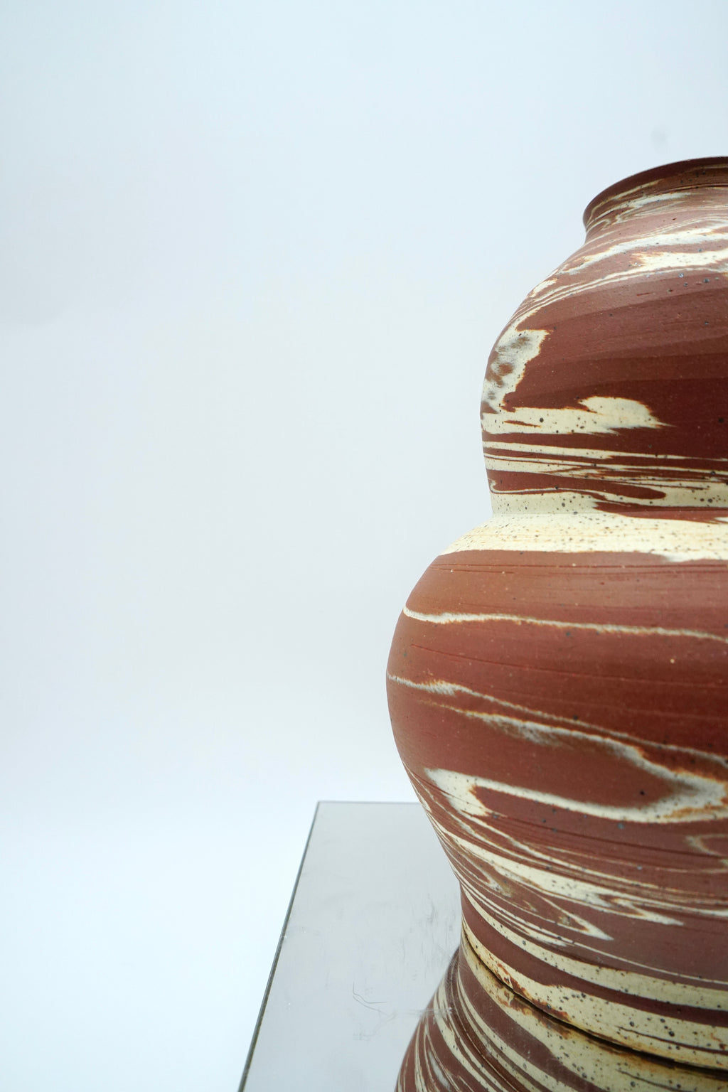 Ceramic vase with marbled brown and beige design on a reflective surface and white background