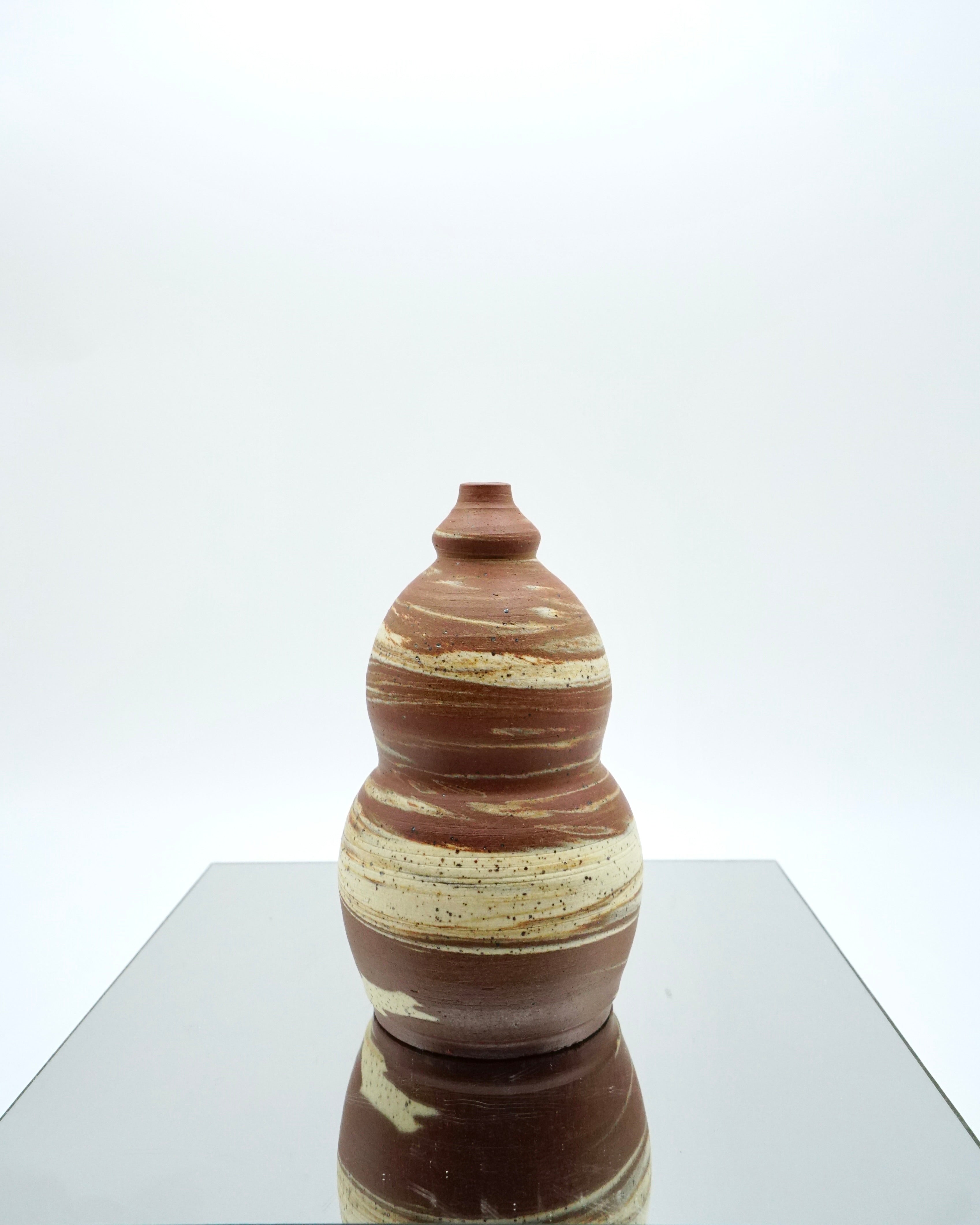 Marbled ceramic vase with brown and beige pattern on a reflective surface and white background