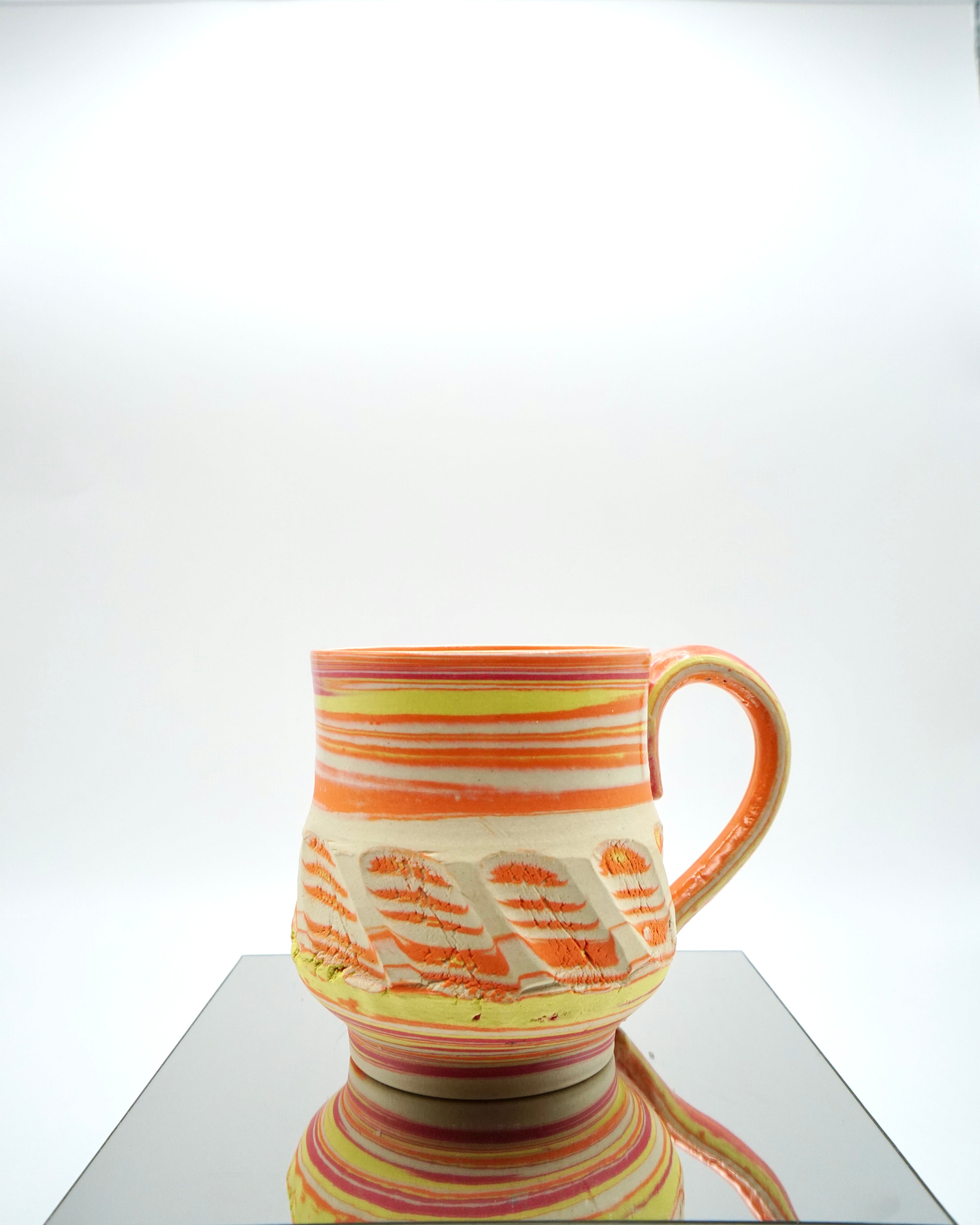 Ceramic mug with red, orange, yellow, white swirled patterns on a reflective surface and white background.