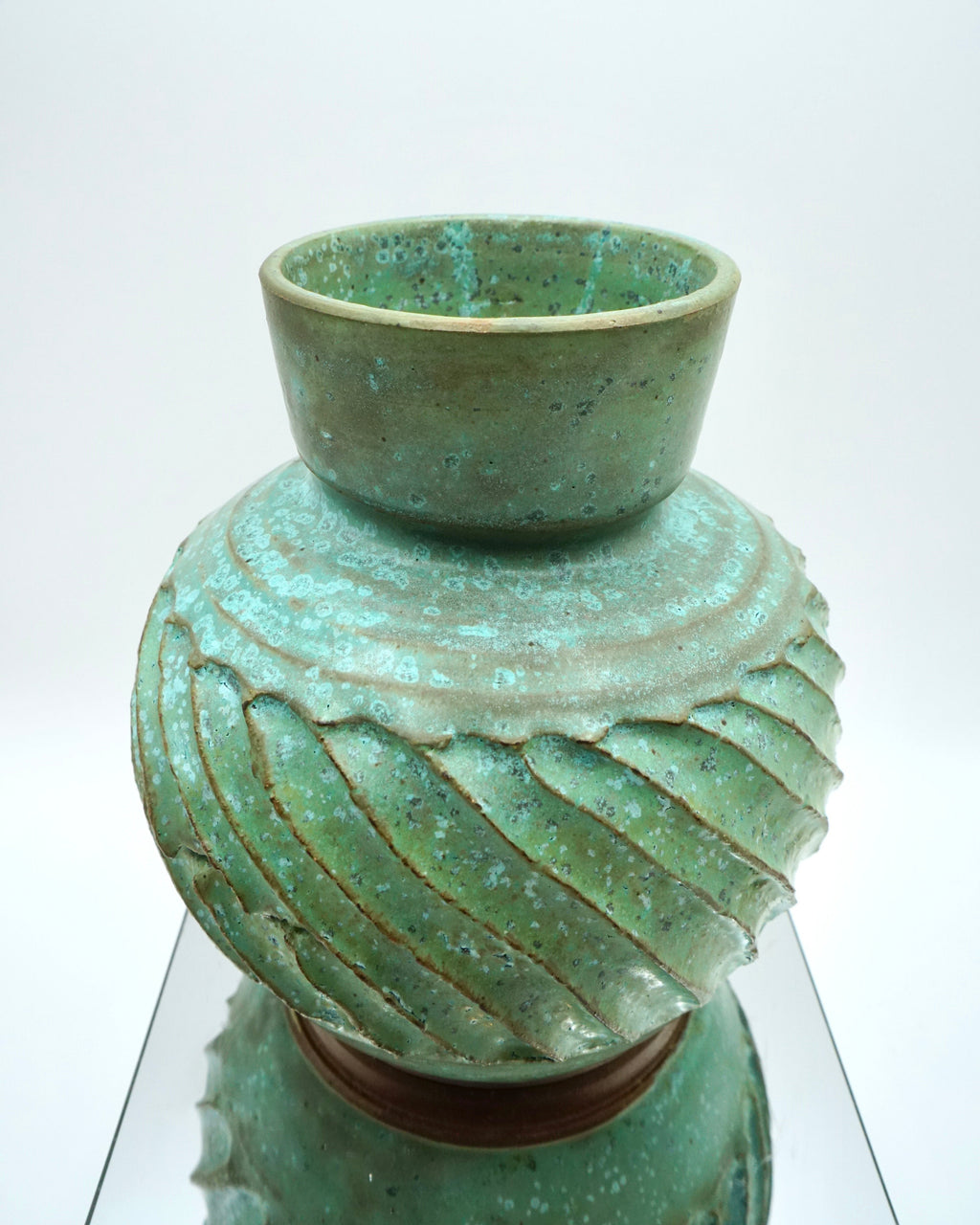 Green ceramic vase with textured design on a reflective surface and white background