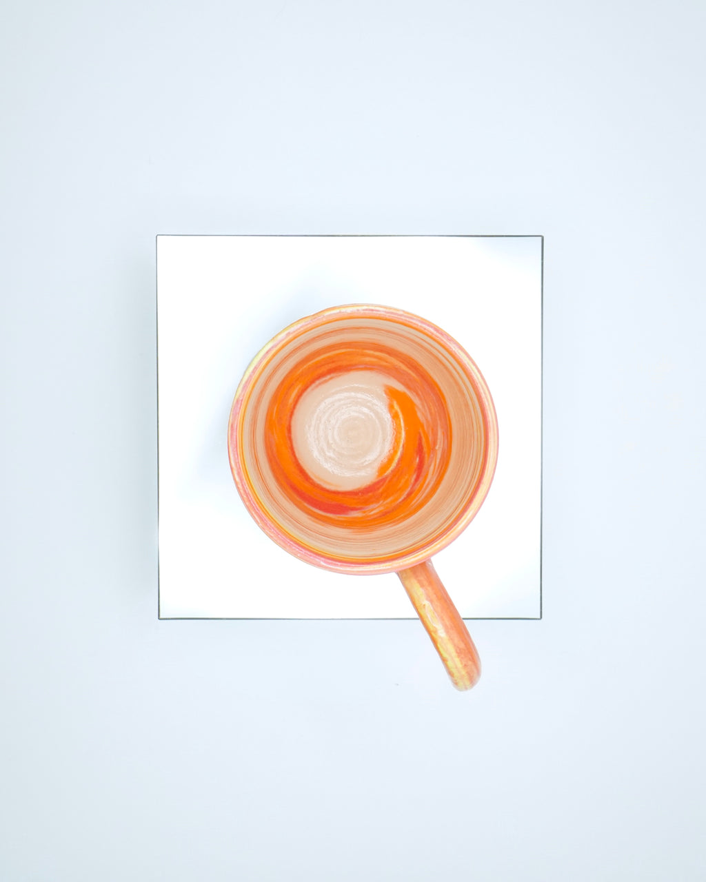 Ceramic cup with red, orange, yellow, white swirled patterns and chrome glaze on a reflective surface and white background.