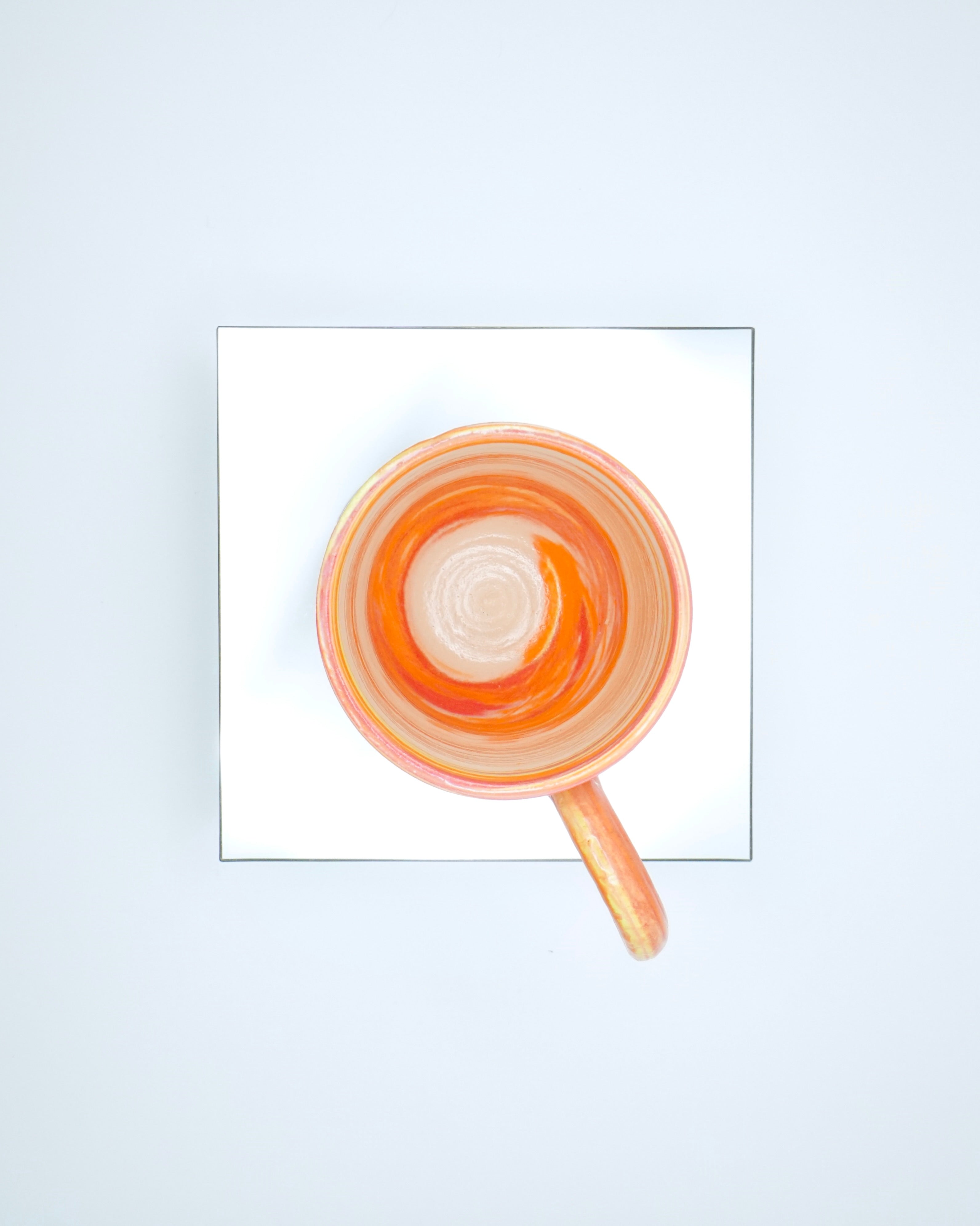 Ceramic cup with red, orange, yellow, white swirled patterns and chrome glaze on a reflective surface and white background.
