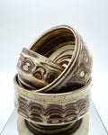 Stack of ceramic bowls with brown and speckled white patterns on a reflective surface and white background.
