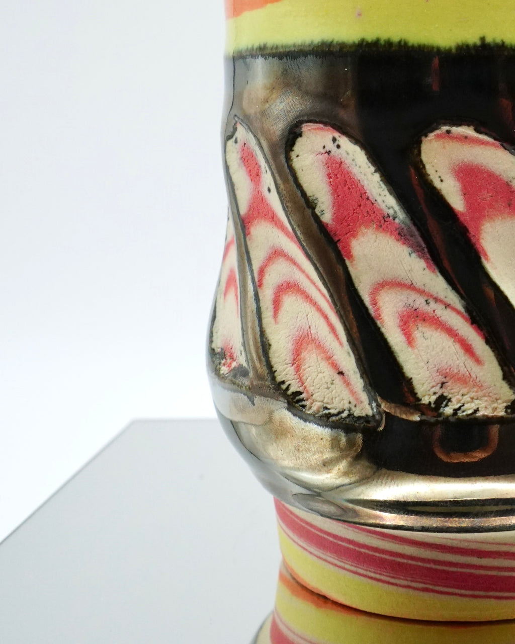 Decorative cup with colorful abstract patterns and chrome glaze on a reflective surface and white background