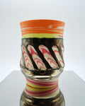 Ceramic cup with red, orange, yellow, white swirled patterns and chrome glaze on a reflective surface and white background.