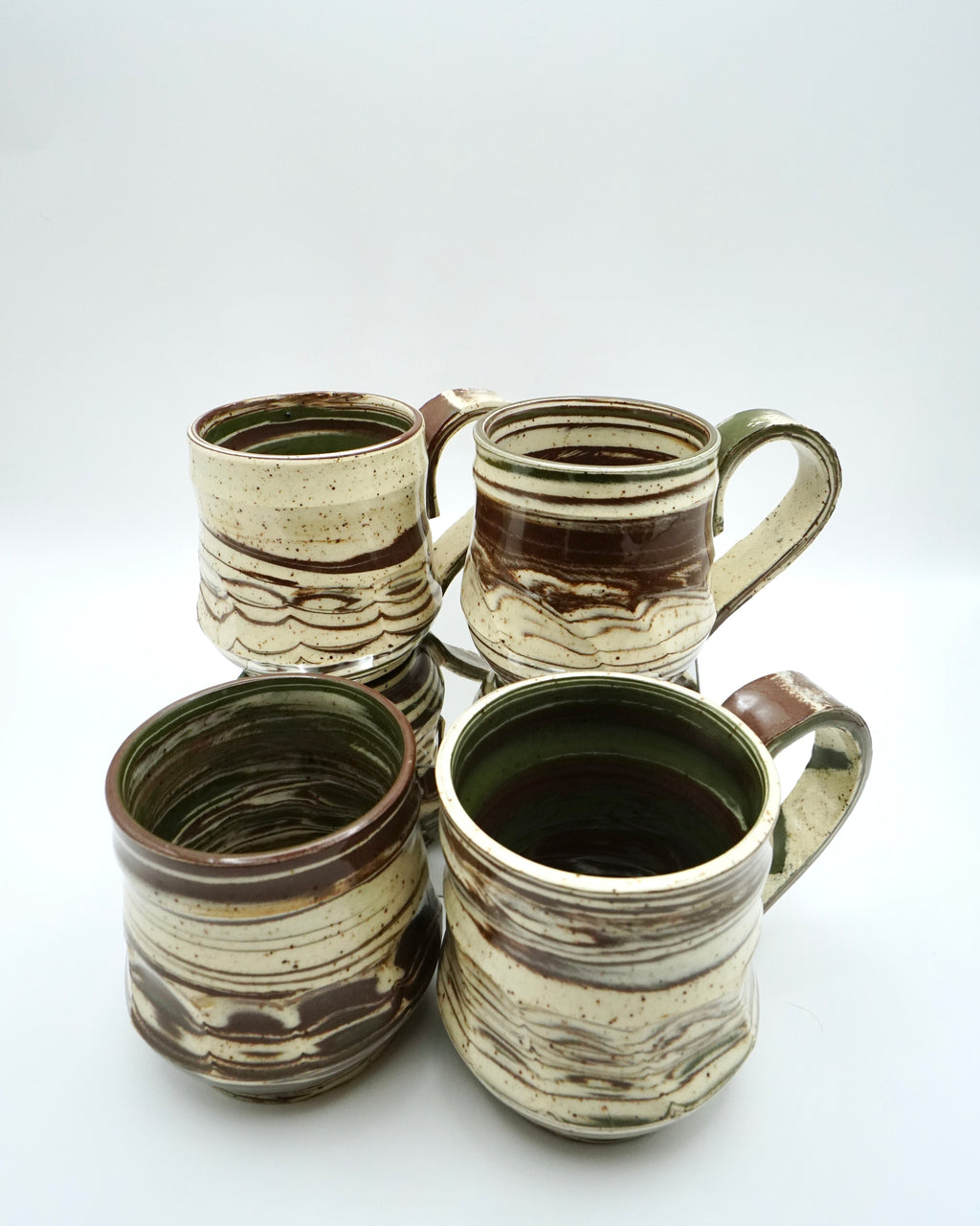 Set of four ceramic mugs with brown, green, and speckled white abstract patterns on a white background.