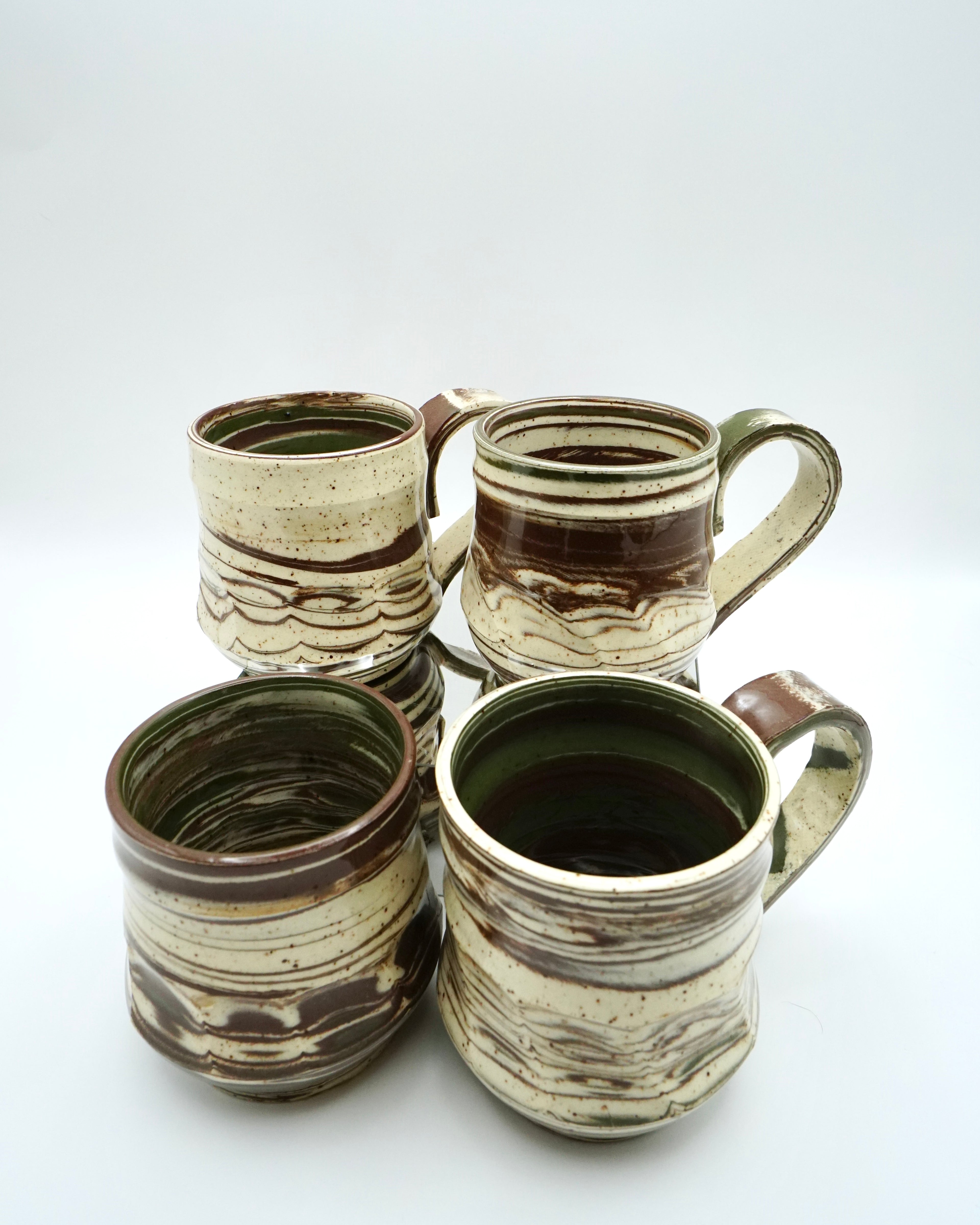 Set of four ceramic mugs with brown, green, and speckled white abstract patterns on a white background.