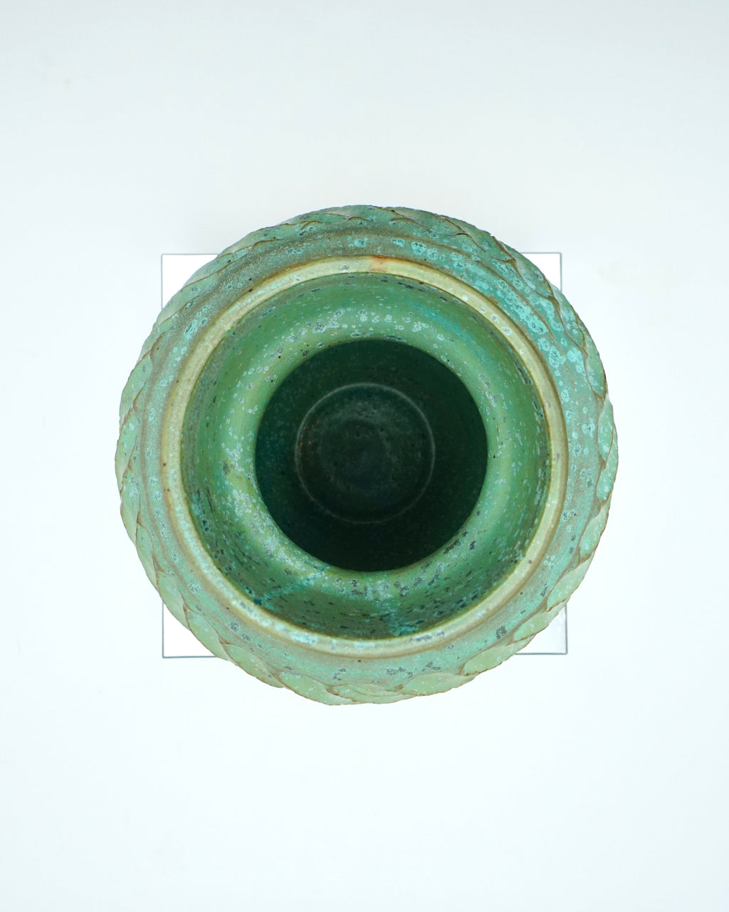 Green ceramic vase with textured design on a reflective surface and white background