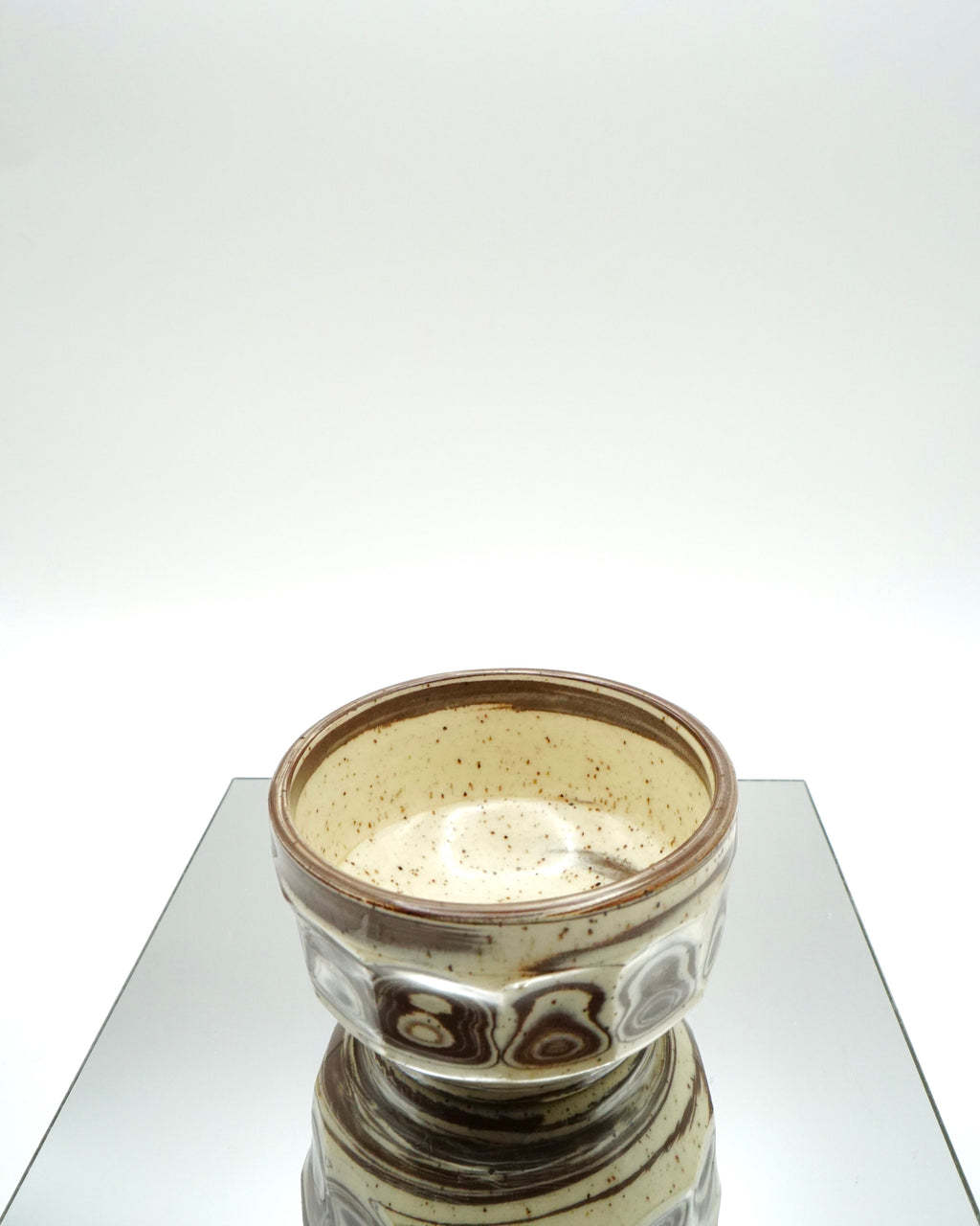 Ceramic bowl with brown and speckled white patterns on a reflective surface and white background.