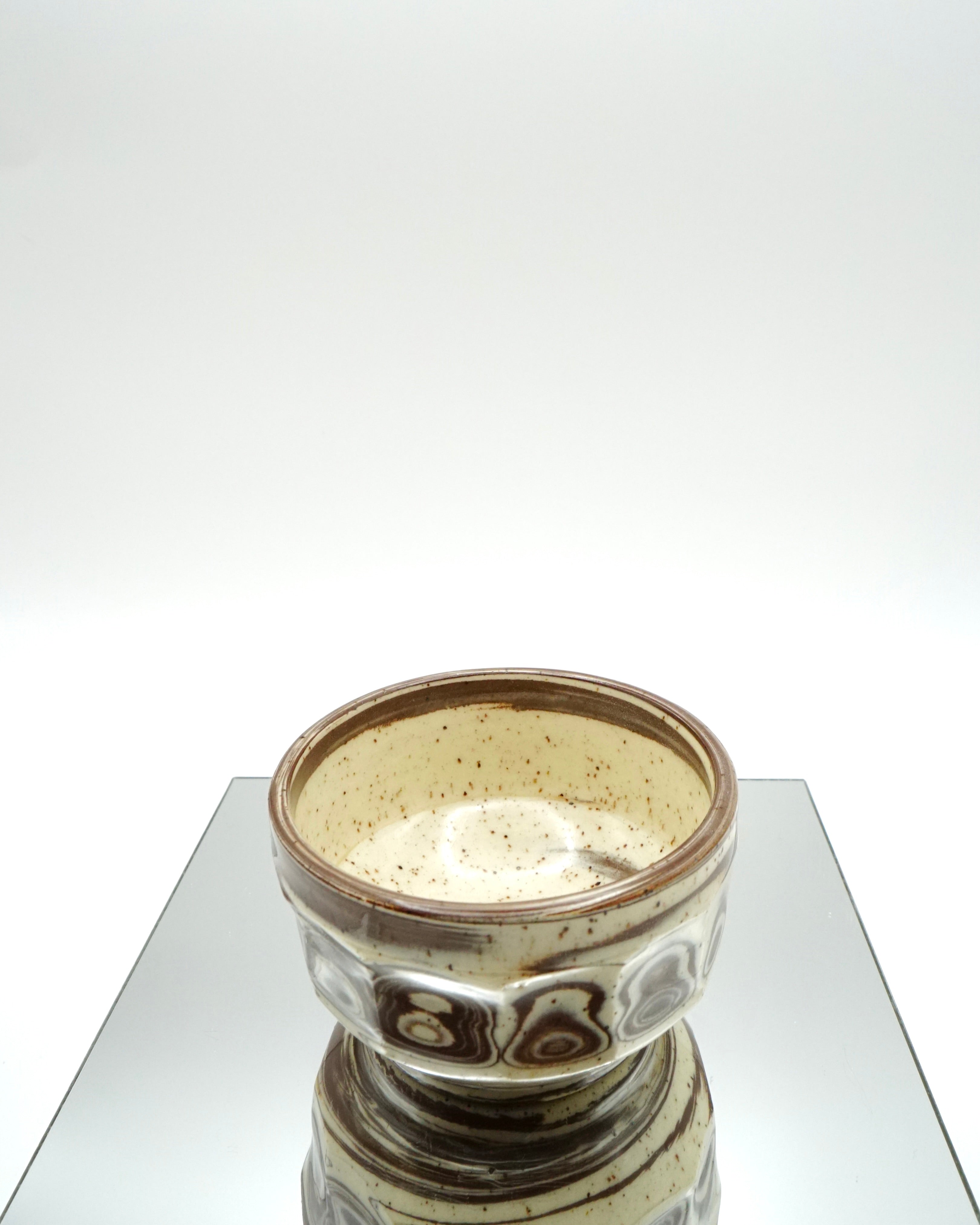Ceramic bowl with brown and speckled white patterns on a reflective surface and white background.