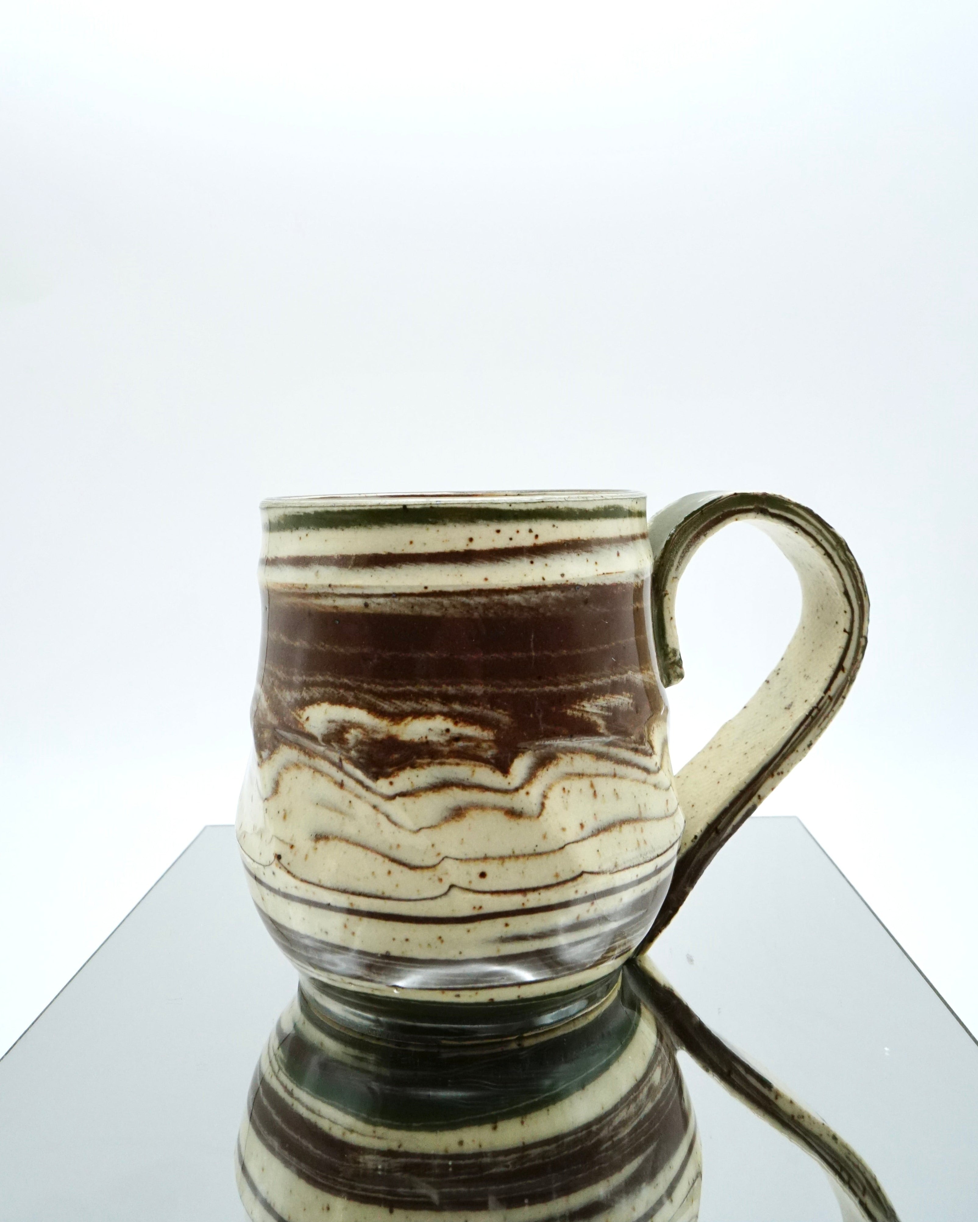 Ceramic mug with brown, green, and speckled white abstract patterns on a reflective surface and white background.