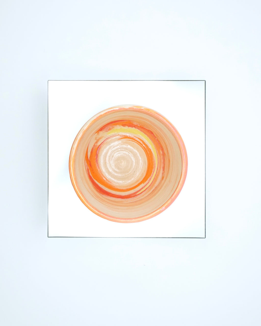 Ceramic cup with red, orange, yellow, white swirled patterns on a reflective surface and white background.