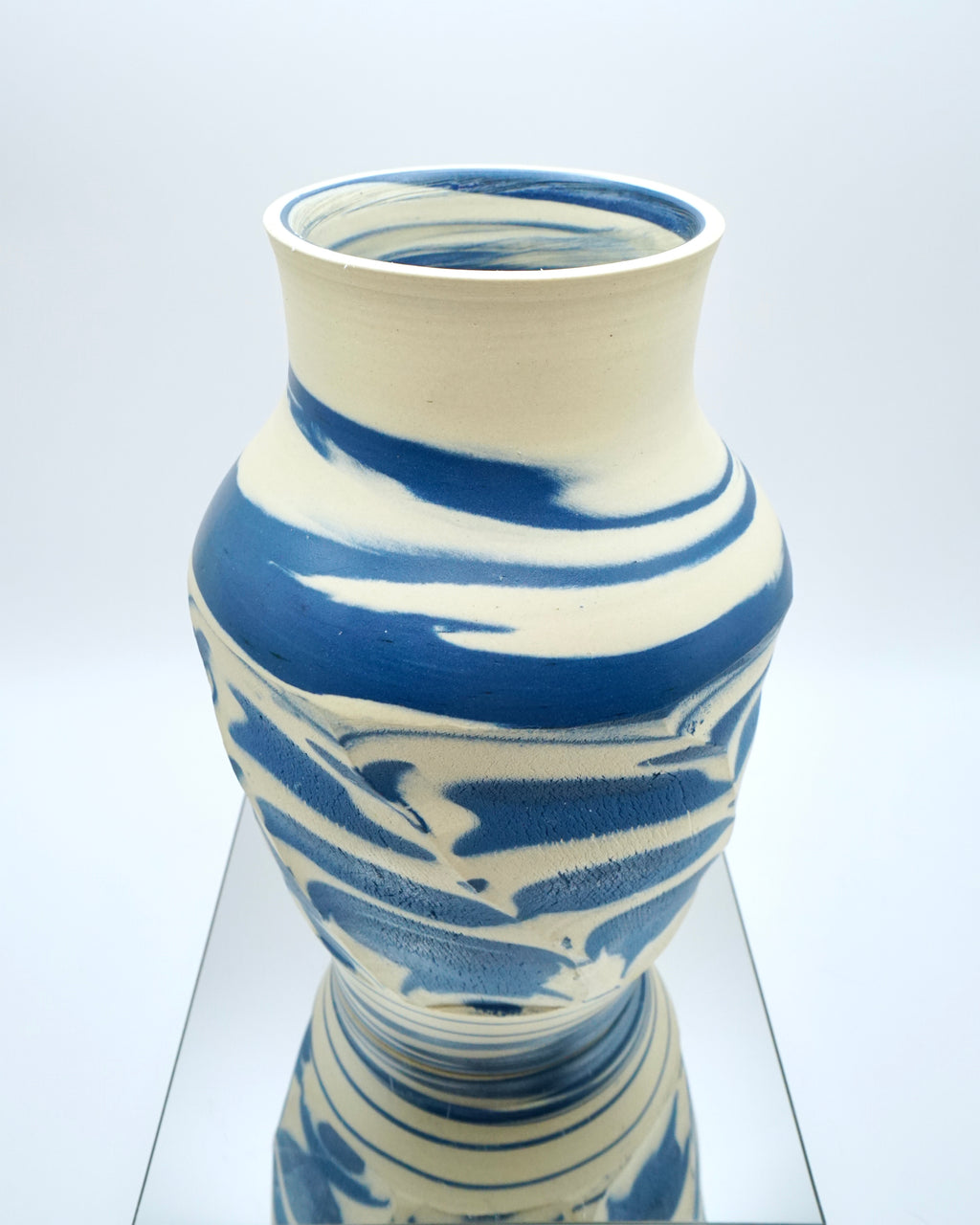 Ceramic vase with blue and white abstract pattern on a reflective surface and white background
