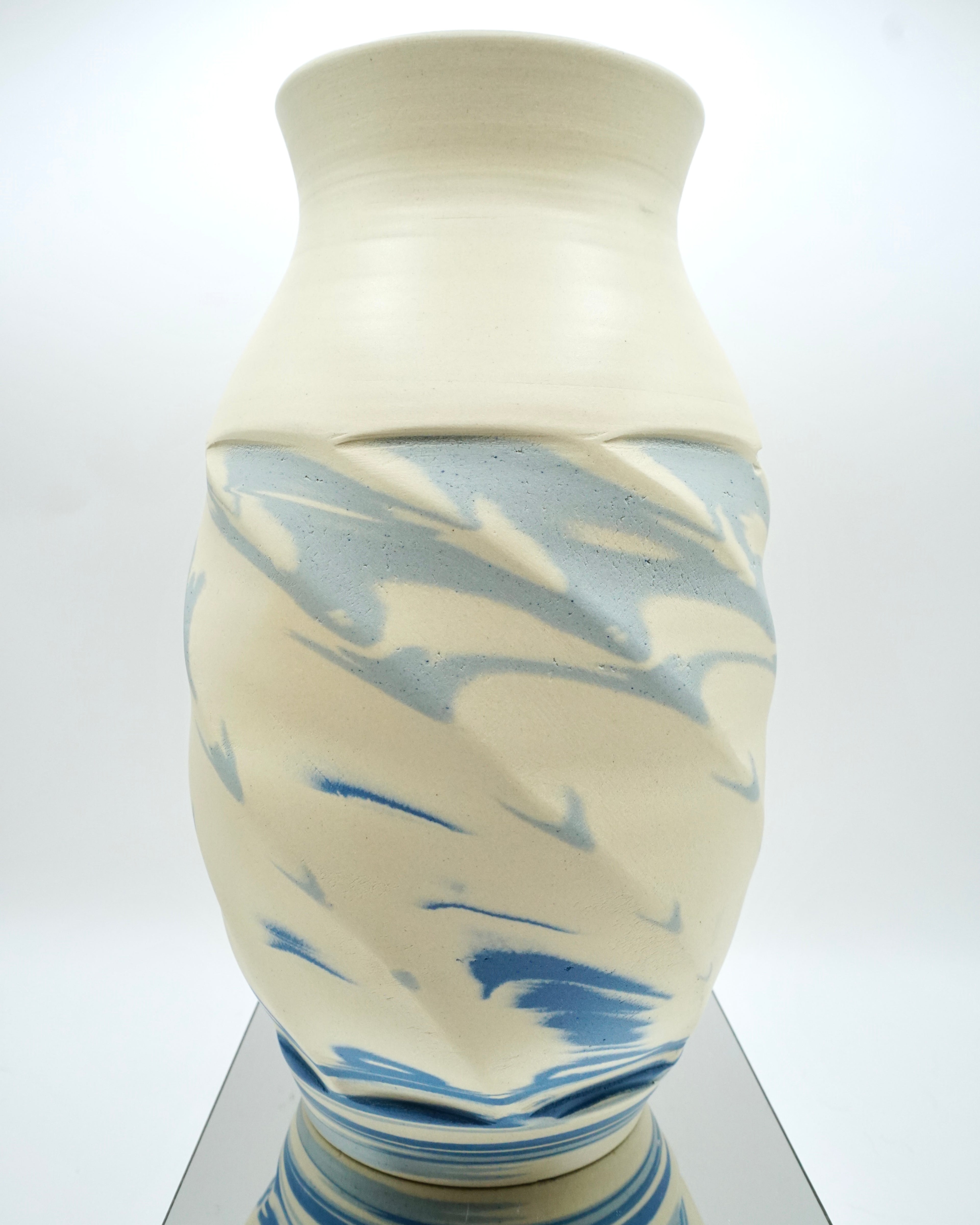 Ceramic vase with blue and white abstract pattern on a reflective surface and white background