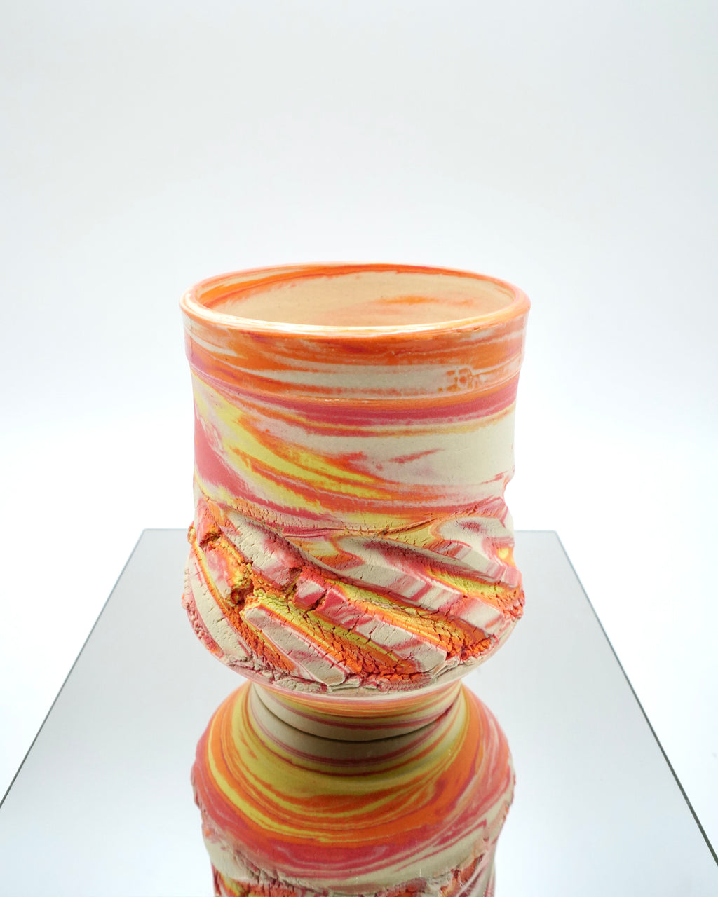 Ceramic cup with red, orange, yellow, white swirled patterns on a reflective surface and white background.