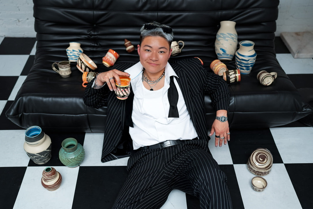 Person in a suit sitting on a black leather couch with decorative vases around
