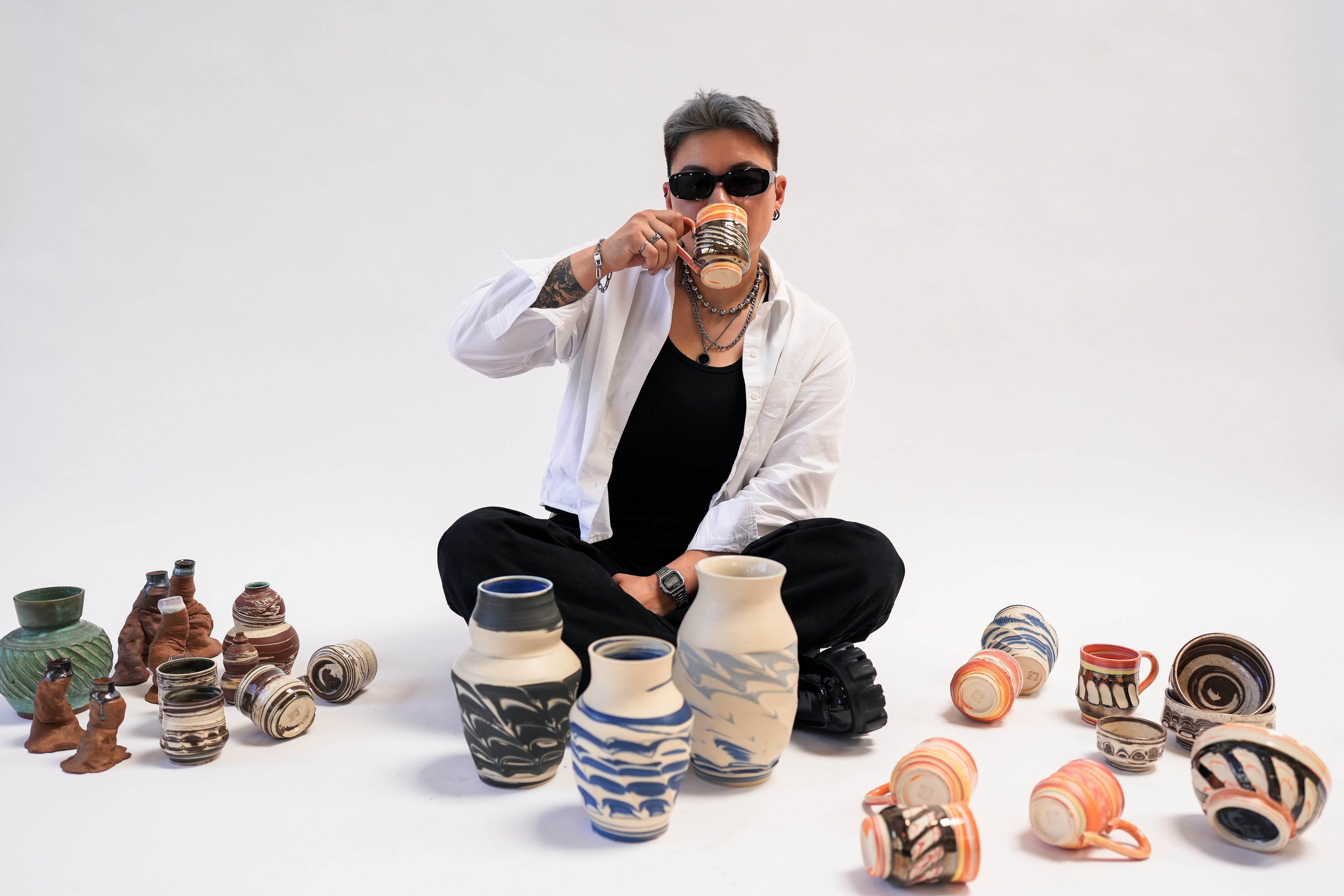 Person sitting among various ceramic pots on a white background